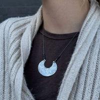 Scoop Necklace displayed on a model wearing a cozy cardigan, showcasing its unique geometric design and adjustable silk cord.