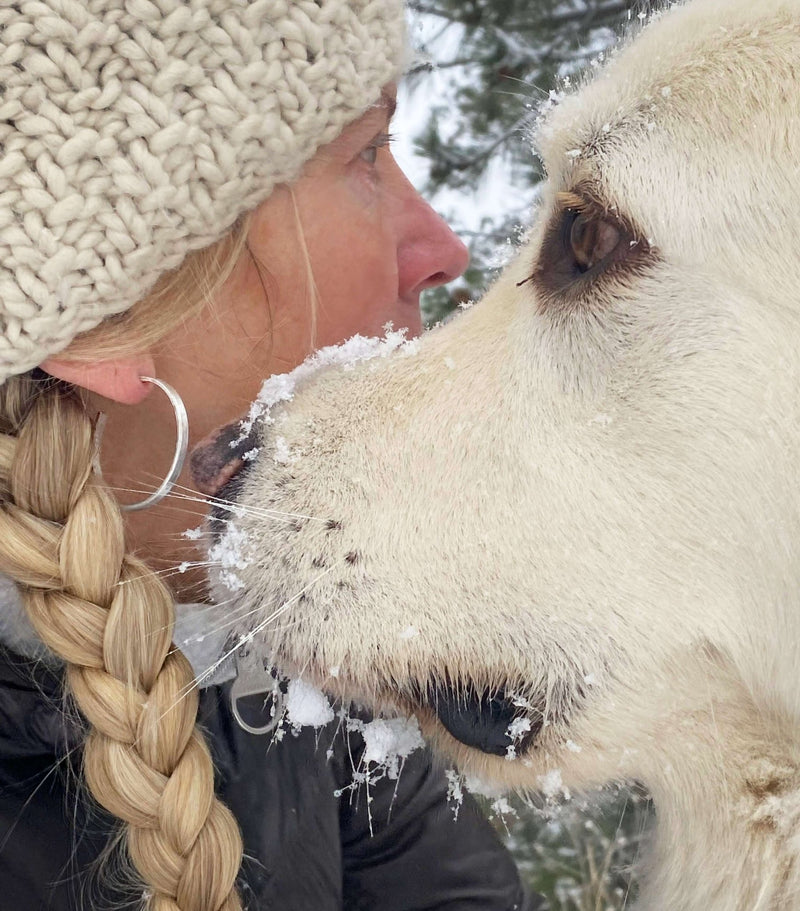 Close-up of woman with a braided hairstyle and a white dog in winter snow.