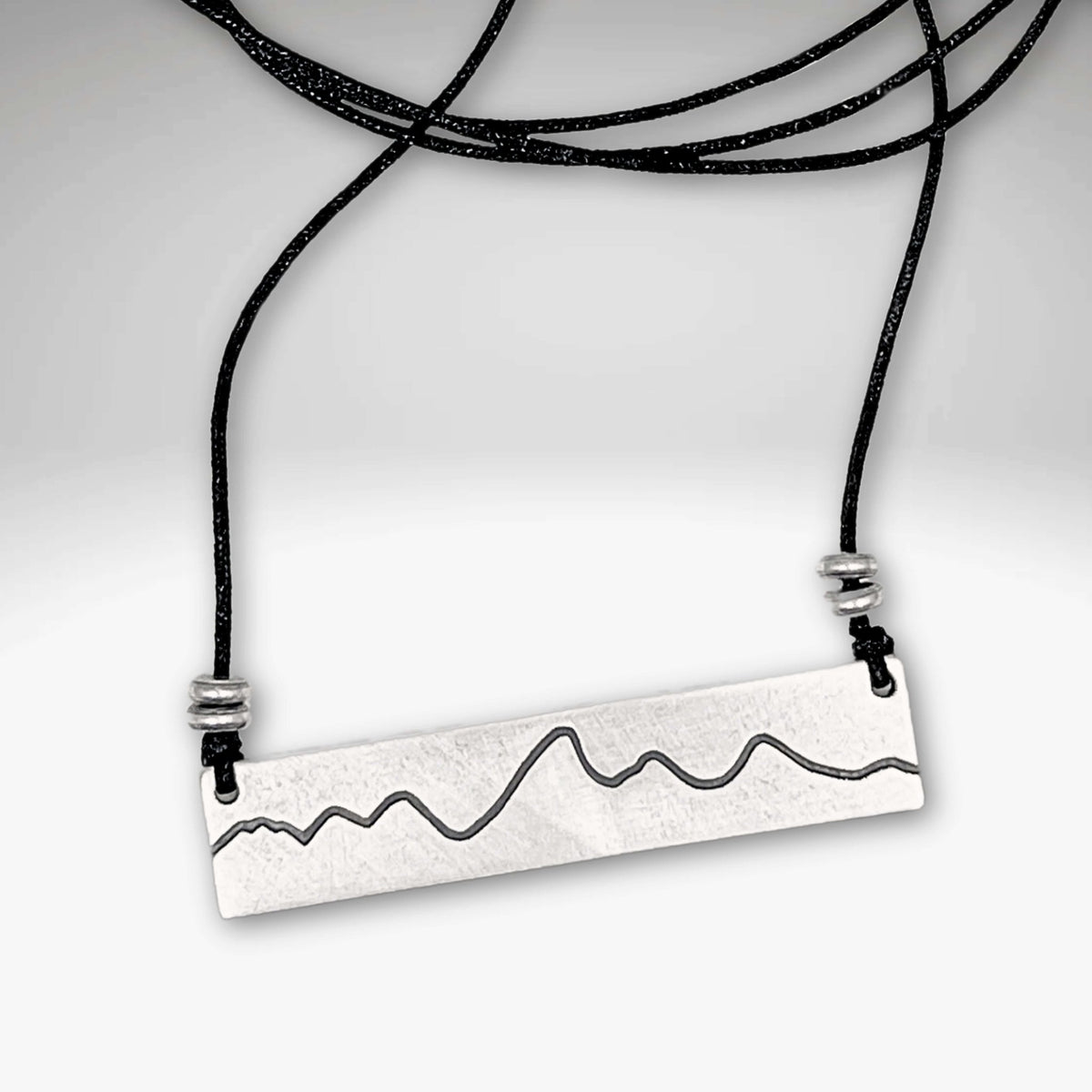 Simple Teton Mountain Necklace featuring an etched brass pendant with a mountain range outline on an adjustable cord.