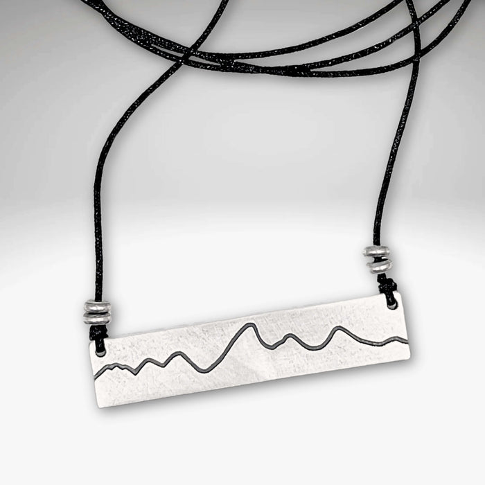 Simple Teton Mountain Necklace featuring an etched brass pendant with a mountain range outline on an adjustable cord.