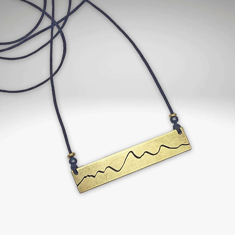 Simple Teton Mountain Necklace featuring a brass pendant with a Teton mountain outline and adjustable navy cord.