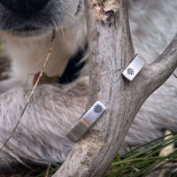 Skinny Bitterroot Flower Cuff Bracelet displayed on a natural branch with a blurred dog in the background.