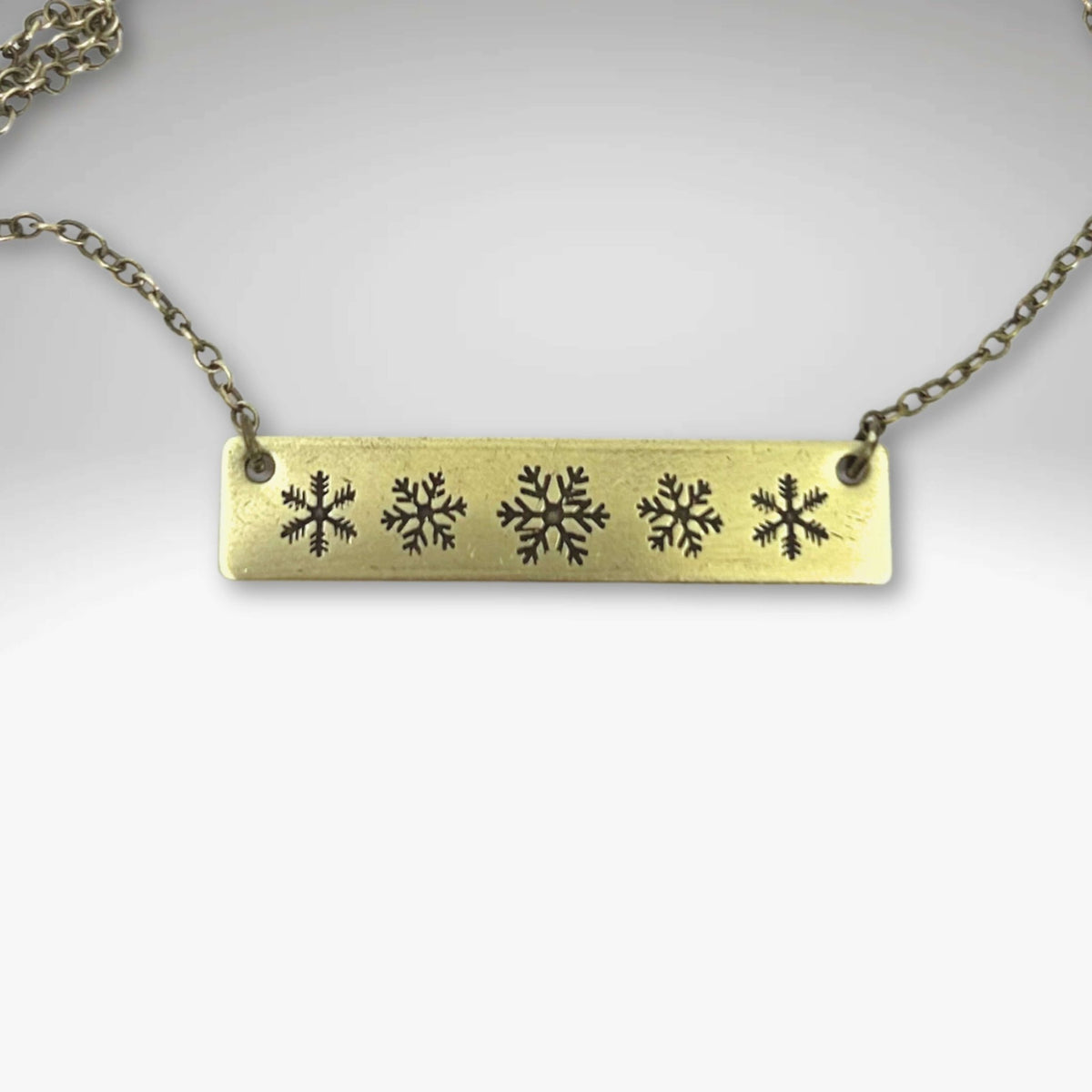Snowfall Necklace featuring a snowflake bar design in antique brass finish on an adjustable chain.