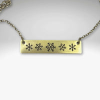 Snowfall Necklace featuring a snowflake bar design in antique brass finish on an adjustable chain.