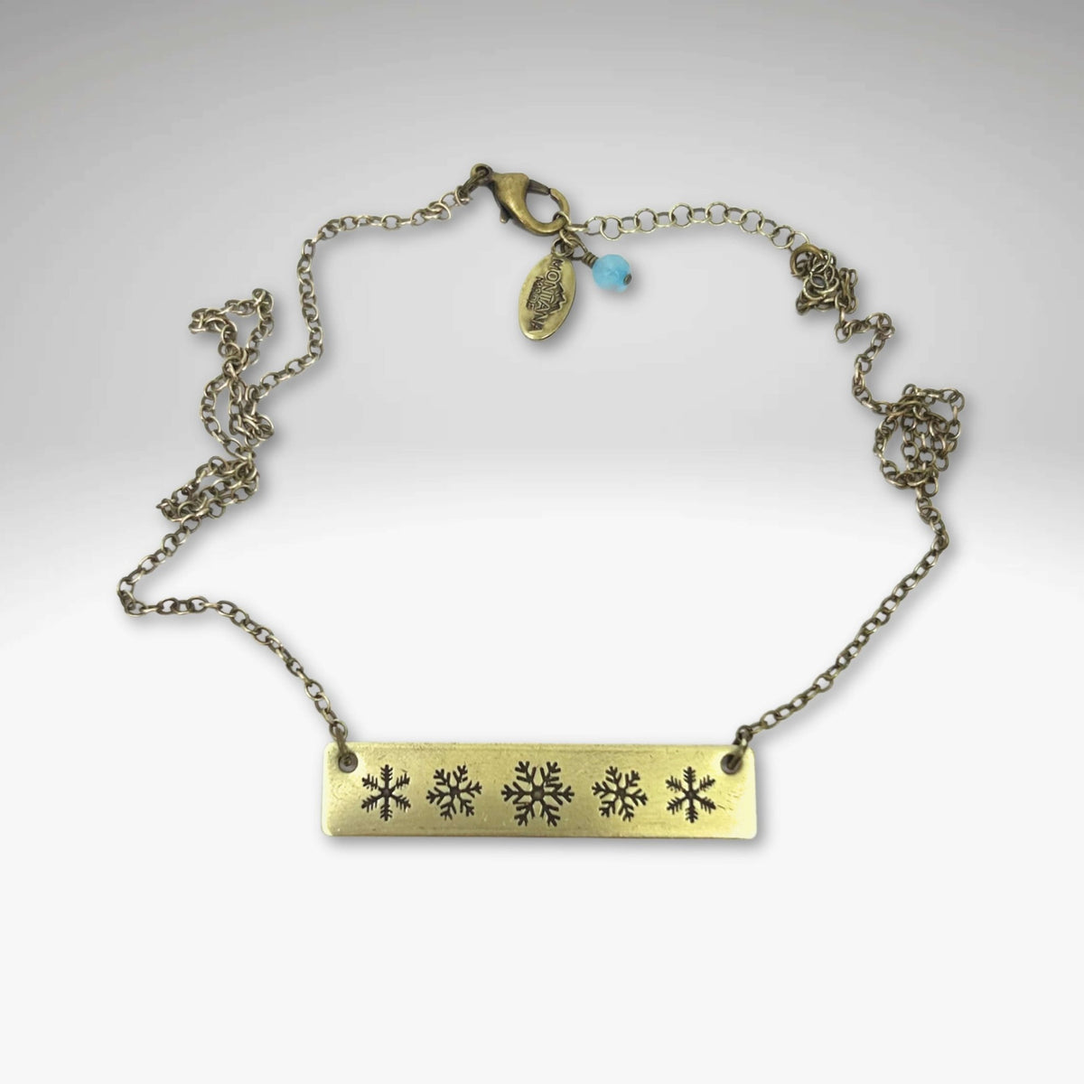 Snowfall Necklace featuring a snowflake bar design on an Antique Brass finish with an adjustable chain.
