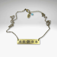 Snowfall Necklace featuring a snowflake bar design on an Antique Brass finish with an adjustable chain.