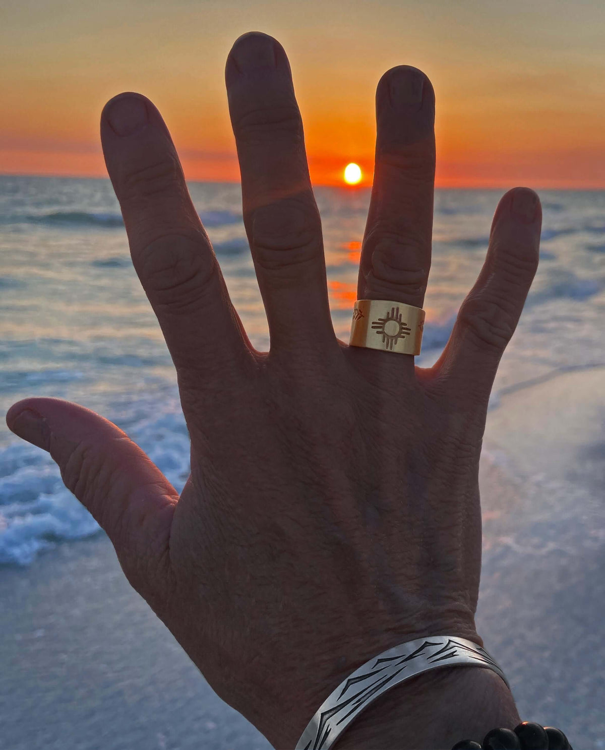 Person wearing Sol Adjustable Ring, showcasing Zia sun design against a stunning sunset backdrop.