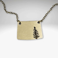 Spruce Necklace featuring a unique pendant design with a tree silhouette on an antique brass finish.