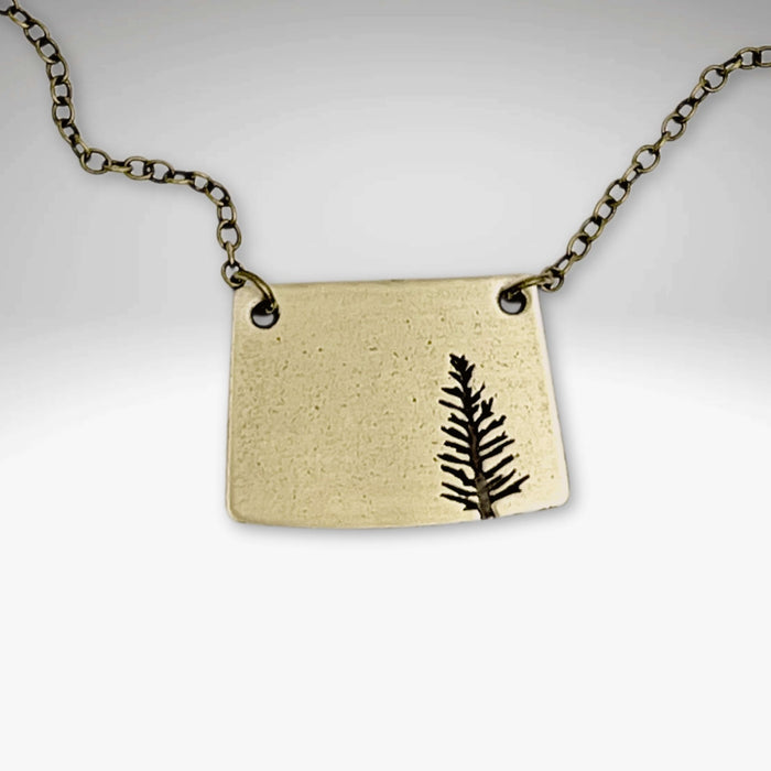 Spruce Necklace featuring a unique pendant design with a tree silhouette on an antique brass finish.