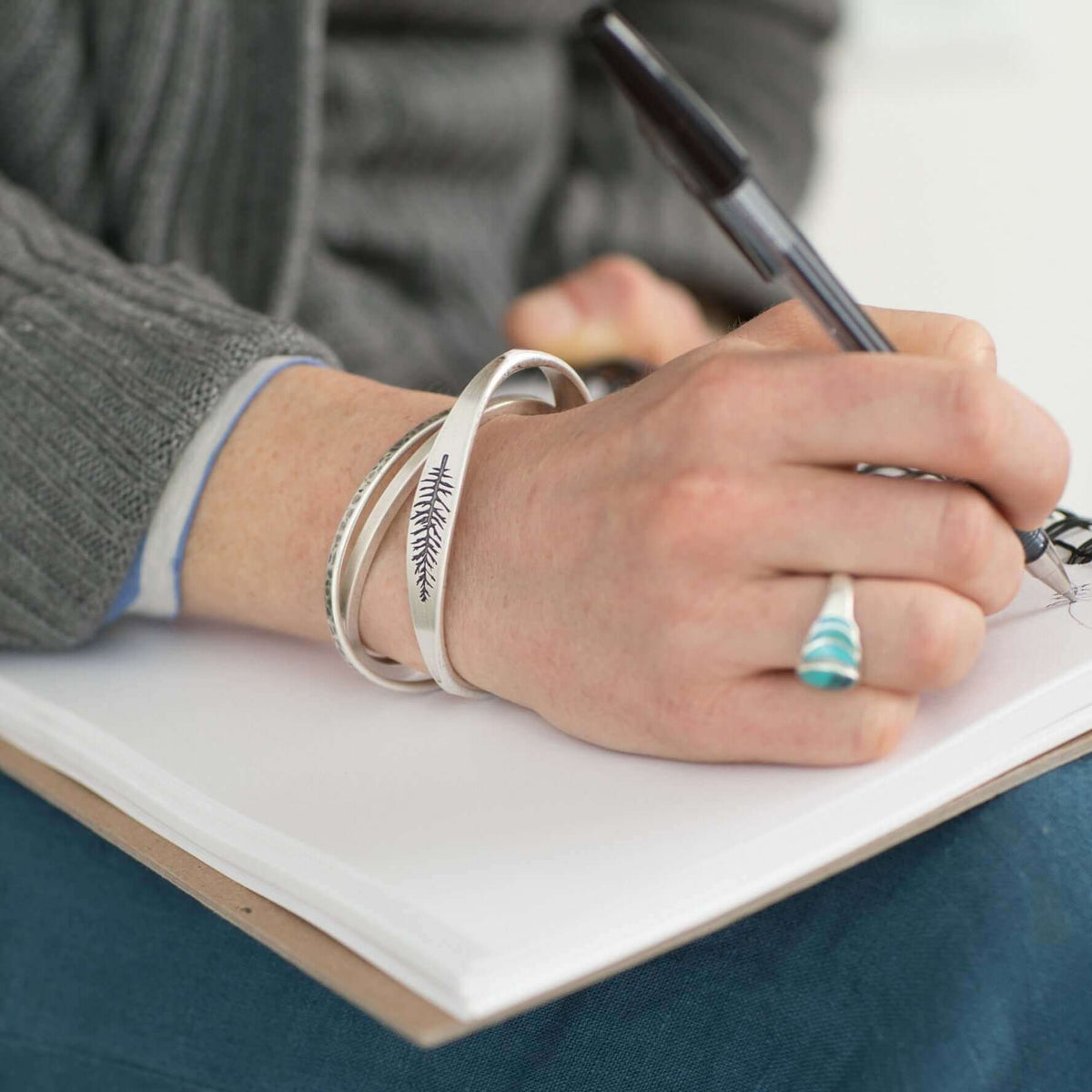 Person wearing the Spruce Signet Cuff Bracelet while writing in a notebook, showcasing the natural design.