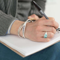 Person wearing the Spruce Signet Cuff Bracelet while writing in a notebook, showcasing the natural design.