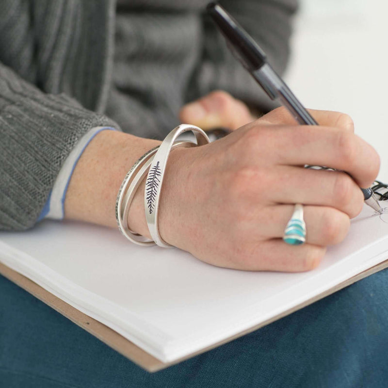 Person wearing the Spruce Signet Cuff Bracelet while writing in a notebook, showcasing the natural design.