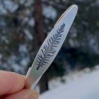 Spruce Signet Cuff Bracelet showcasing a spruce outline etching, held outdoors in nature.