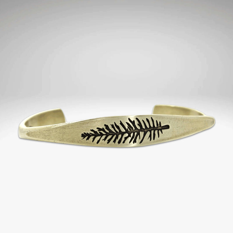 Spruce Signet Cuff Bracelet showcasing a detailed spruce outline etching on a tapered gold cuff.