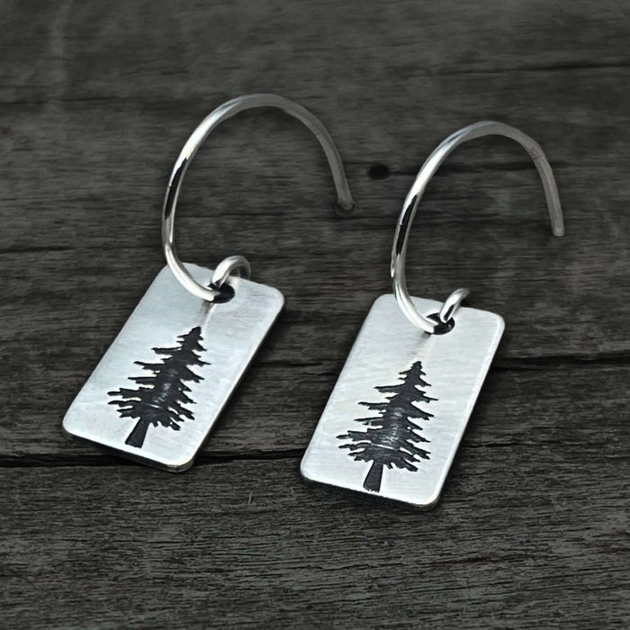 Spruce Tree Hoop Earrings with silver hoops and small spruce tree design on rounded rectangle.