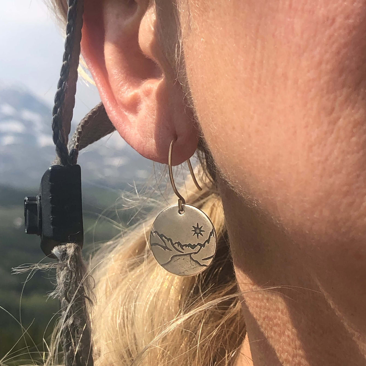 St. Mary Lake Earrings - Glacier Mountain and Lake with Sun worn by a model, showcasing detailed brass etching.