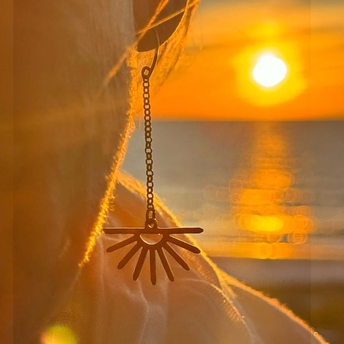Sunbeam Earrings featuring delicate sunray design, swinging on a rolo chain against a sunset backdrop.