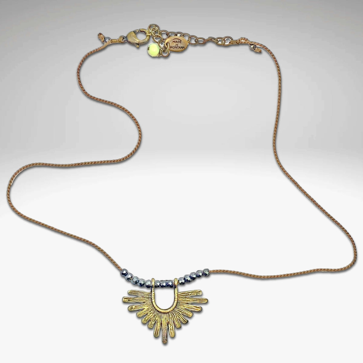 Sunbeam Necklace featuring a geometric pendant and small hematite beads on a delicate silk cord.