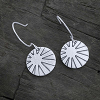Sunrays Earrings featuring silver discs with a sunray design, elegantly hanging from rounded earwires.