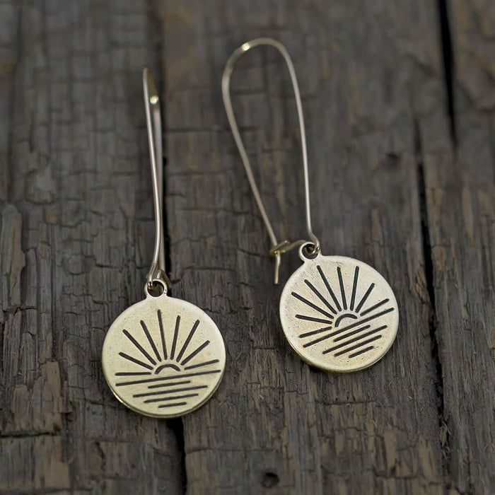Sunrise Earrings featuring a small disc with an etched sunrise and kidney earwire on rustic wood background.