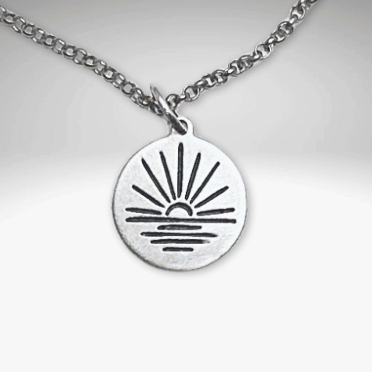 Sunrise Necklace featuring a sun rising over water on a silver pendant with an adjustable chain.