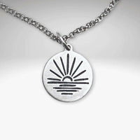 Sunrise Necklace featuring a sun rising over water on a silver pendant with an adjustable chain.