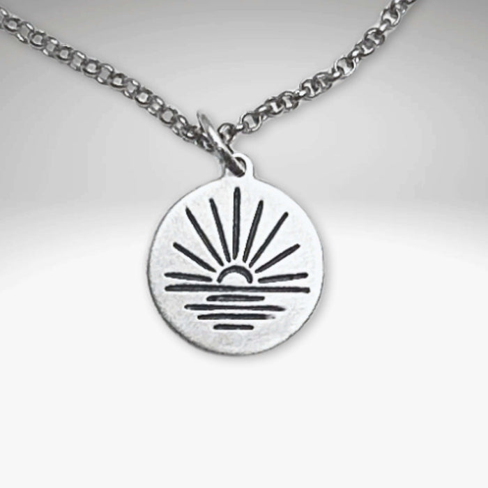 Sunrise Necklace featuring a sun rising over water on a silver pendant with an adjustable chain.