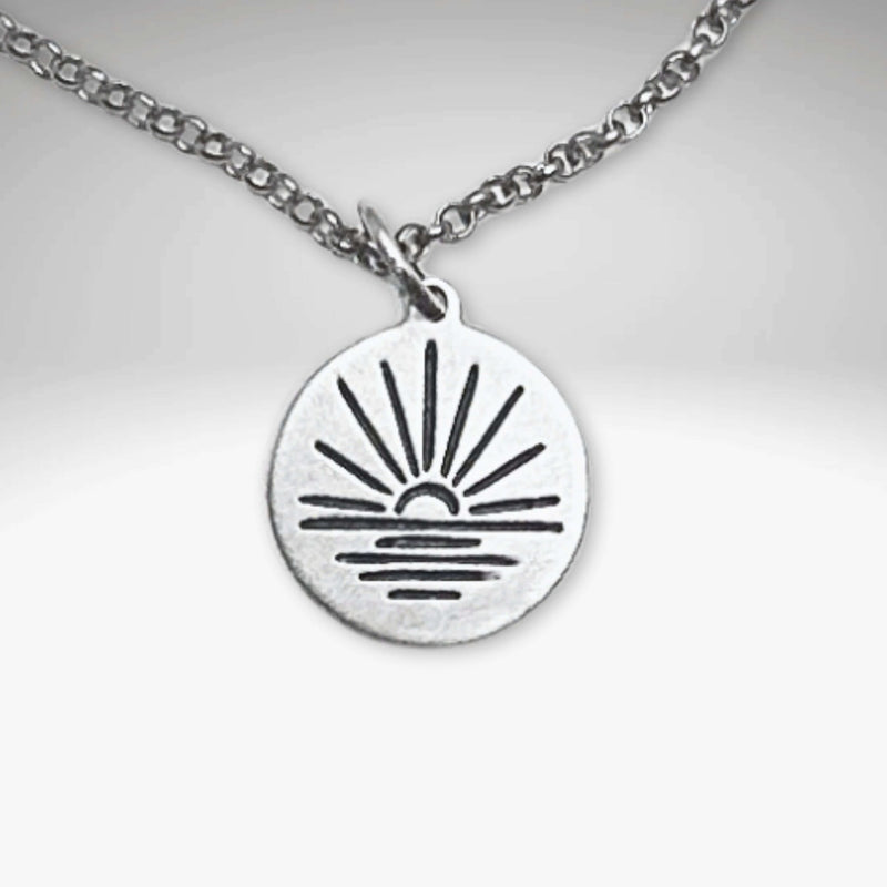 Sunrise Necklace featuring a sun rising over water on a silver pendant with an adjustable chain.
