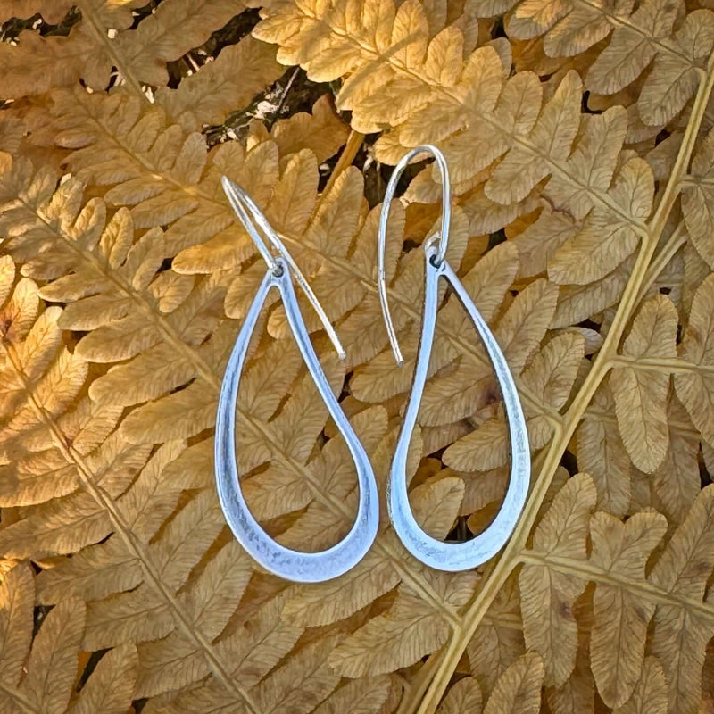 Lightweight Matte Silver Teardrop Earrings on a leaf background, showcasing their elegant design and texture.