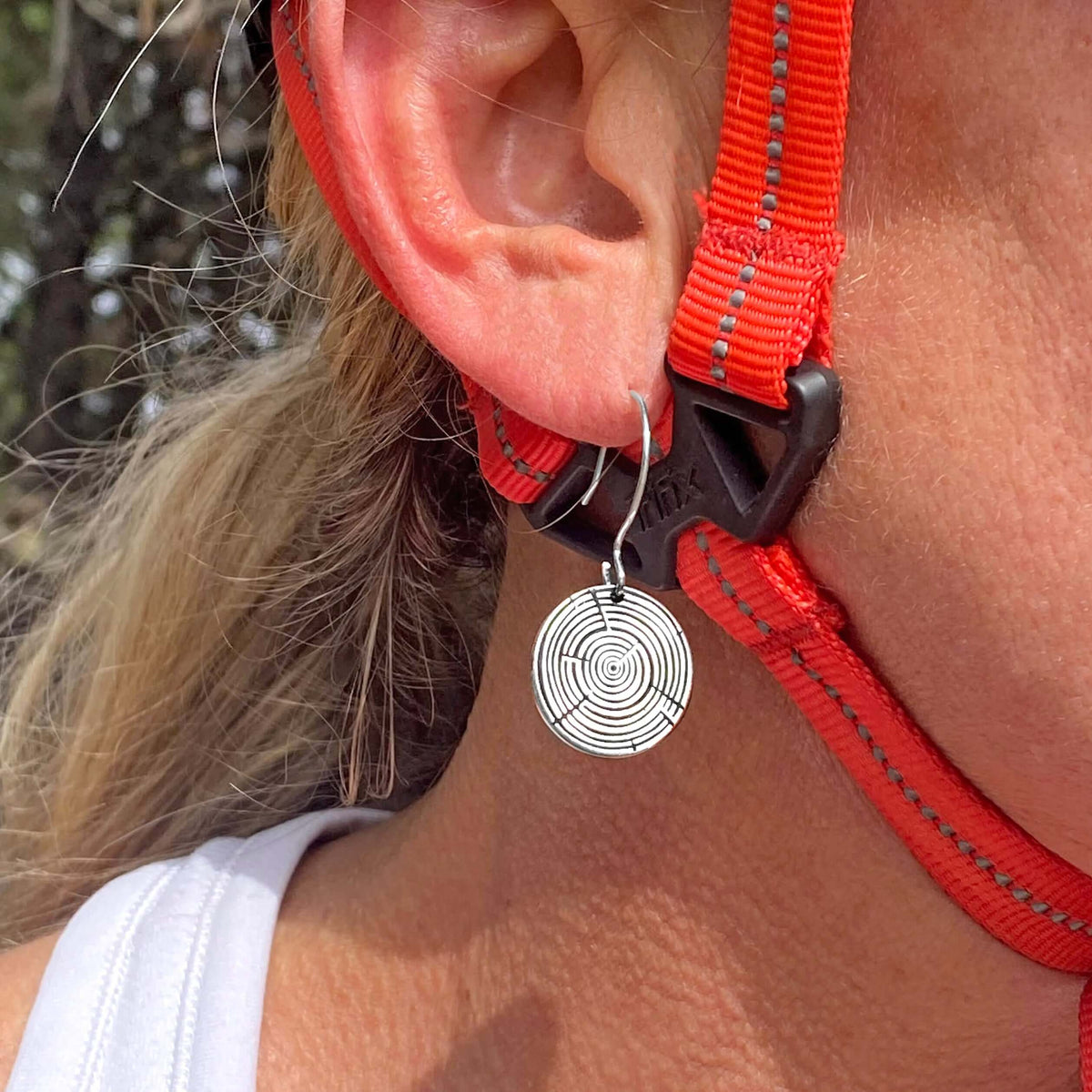 Model wearing Timber Earrings- Tree Rings, showcasing silver circular design near ear with outdoor backdrop.