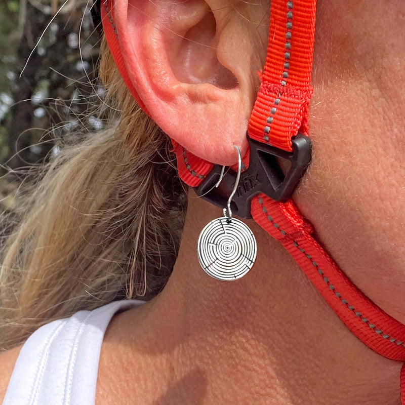 Model wearing Timber Earrings- Tree Rings, showcasing silver circular design near ear with outdoor backdrop.