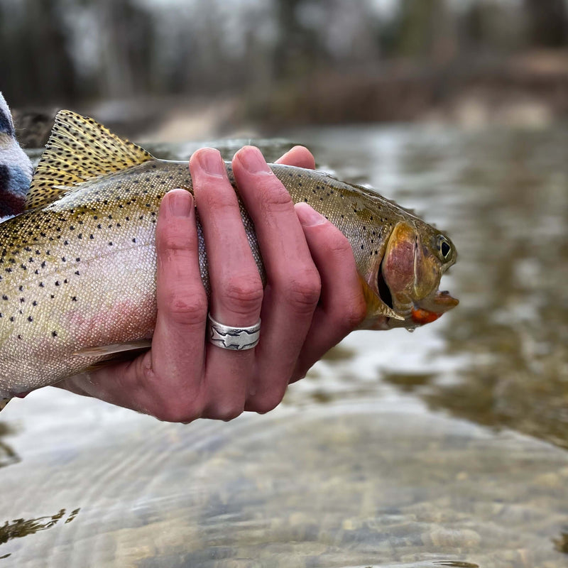 Person holding a trout while wearing a Trout Ring, showcasing the beauty of nature and fishing.