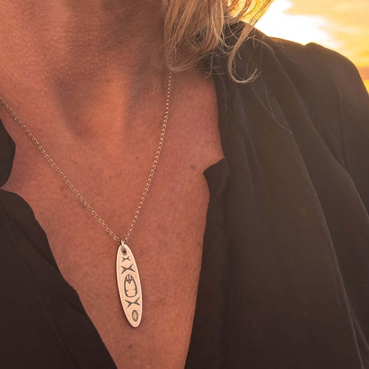 Close-up of the Upstream Necklace with delicate kayak design worn on a woman, showcasing its beauty during sunset.