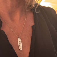 Close-up of the Upstream Necklace with delicate kayak design worn on a woman, showcasing its beauty during sunset.