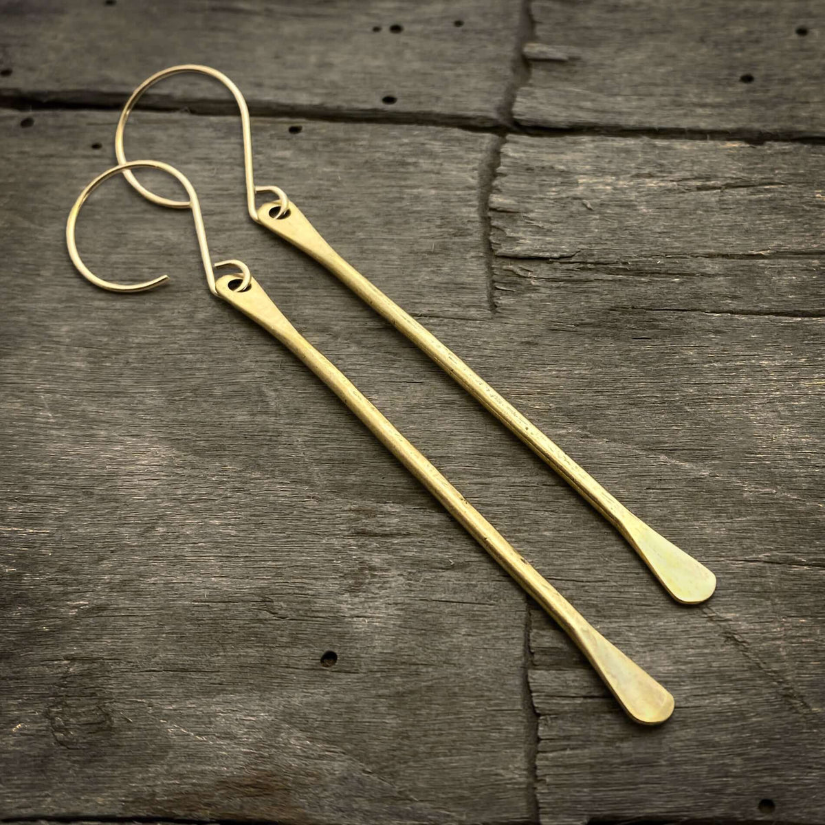 Upstream Paddle Earrings in brass finish hanging on wooden background.