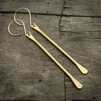 Upstream Paddle Earrings in brass finish hanging on wooden background.