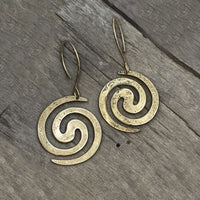 Vortex Earrings in antique brass on wooden background, featuring lightly hammered spiral design.