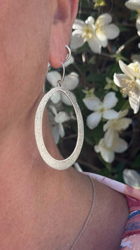 Wide Open Earrings worn by a model, showcasing their elegant silver finish against a floral background.