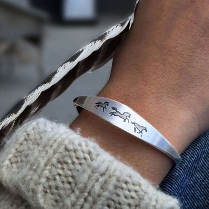Wild Horses Cuff Bracelet showcasing three galloping horses on a matte silver cuff, worn on a cozy sweater.