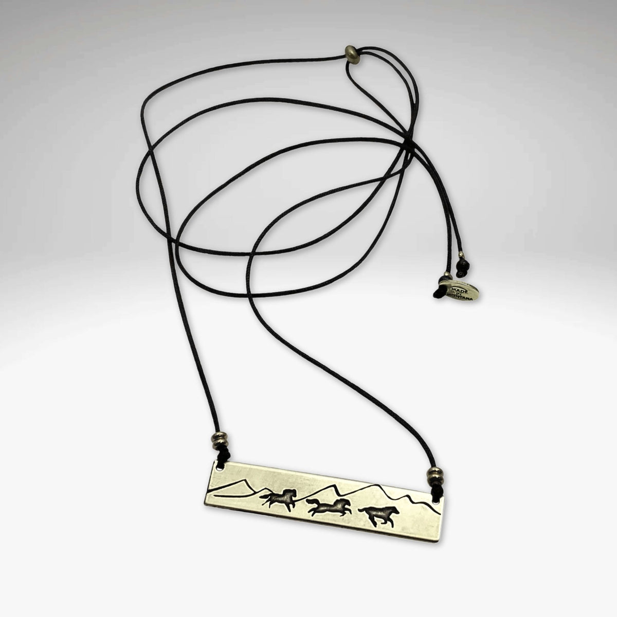 Wild Horses Necklace featuring a brass etching of mustangs and mountains on a cord.