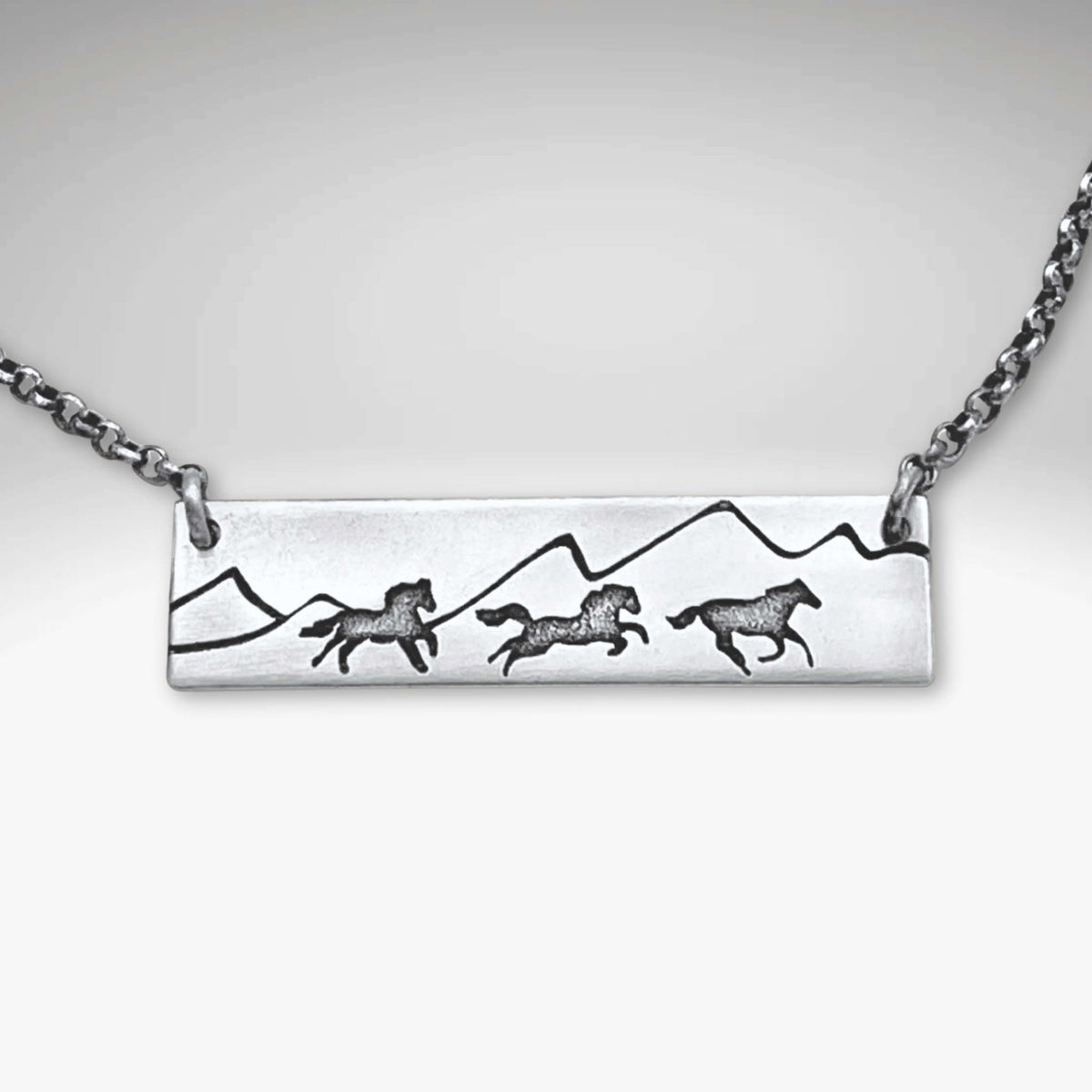 Wild Horses Necklace featuring etched horses and mountains on a silver pendant with a chain.