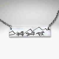 Wild Horses Necklace featuring etched horses and mountains on a silver pendant with a chain.