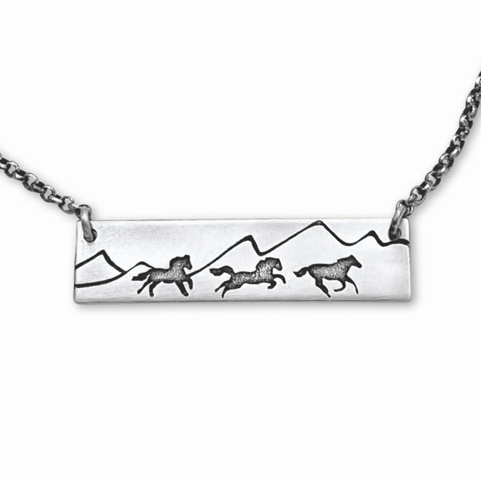 Wild Horses Necklace with etched mountains and galloping horses on a silver chain.