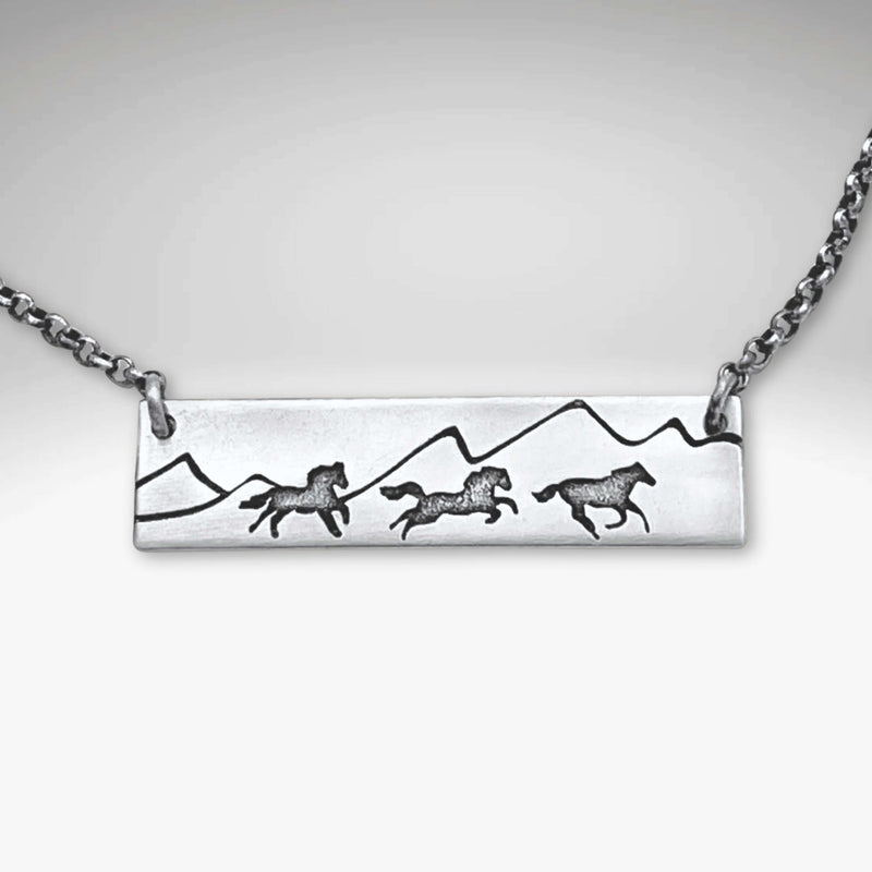 Wild Horses Necklace featuring etched horses and mountains on a silver pendant with a chain.