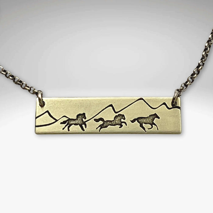 Wild Horses Necklace featuring etched horses and mountains on a brass pendant.
