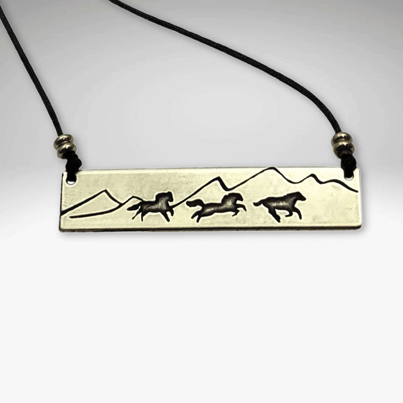 Wild Horses Necklace showcasing etched brass design with running horses and mountains on a strap.