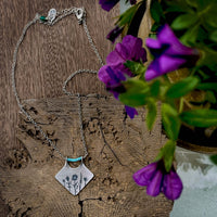 Wildflower Box Necklace featuring floral design and turquoise accents on a wooden background with purple flowers.