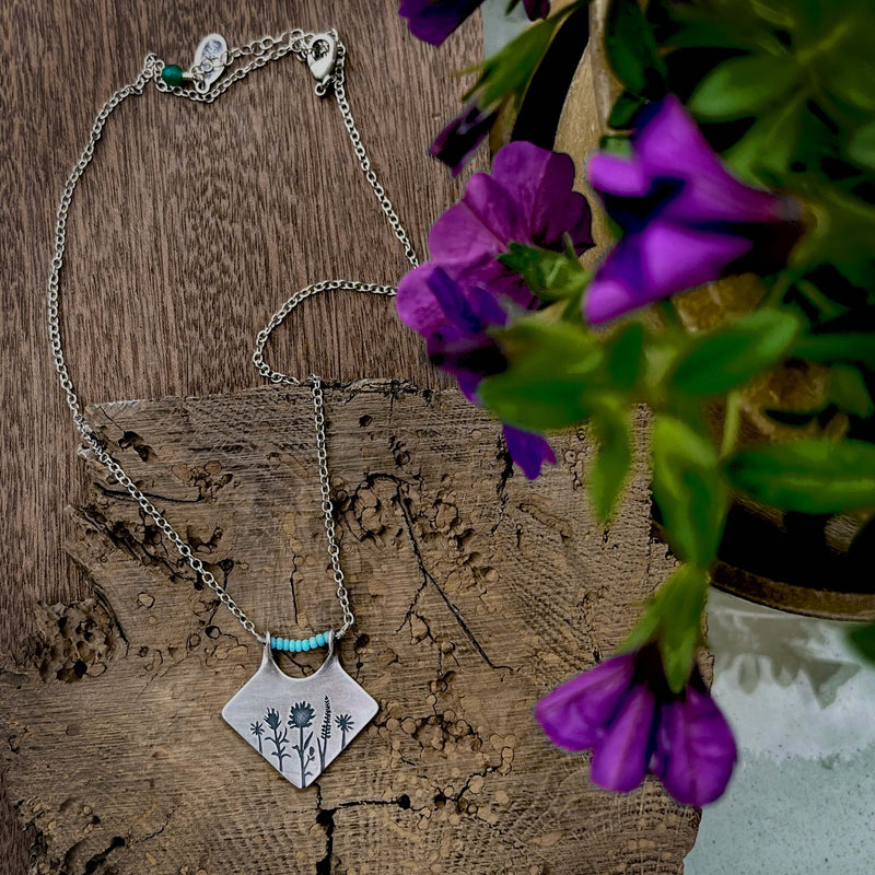 Wildflower Box Necklace featuring floral design and turquoise accents on a wooden background with purple flowers.
