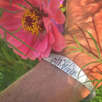 Wildflowers Signet Cuff adorned with floral engravings, worn with vibrant flowers in the background.