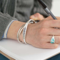 Person wearing three bracelets, including the All Square Cuff Bracelet, while writing in a notebook.